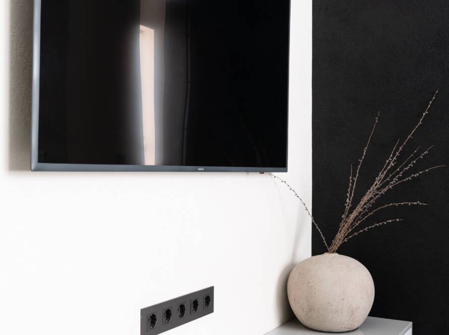 Wall-mounted TV above a white console with a vase of dried grass