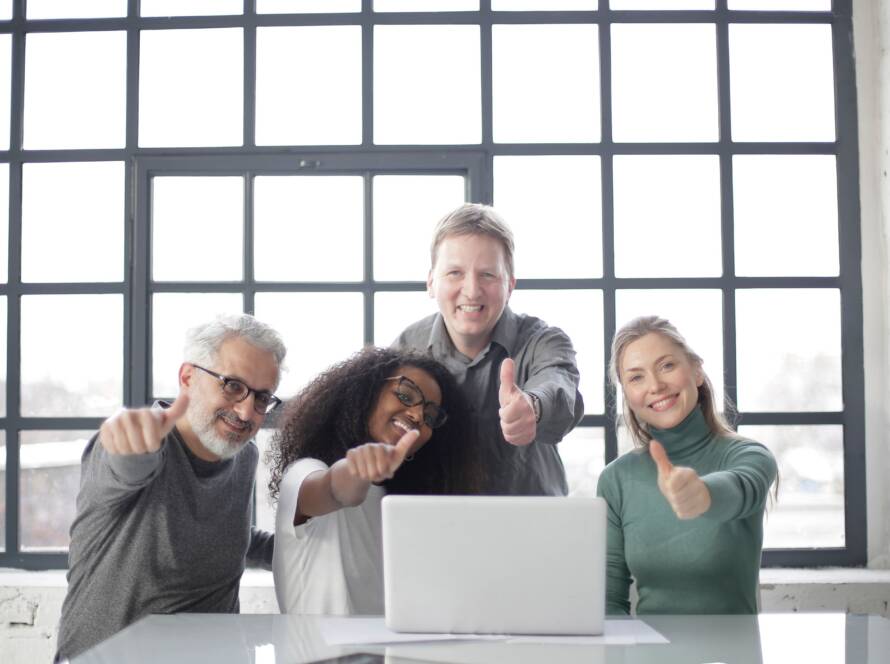Four smiling coworkers giving thumbs up behind a laptop