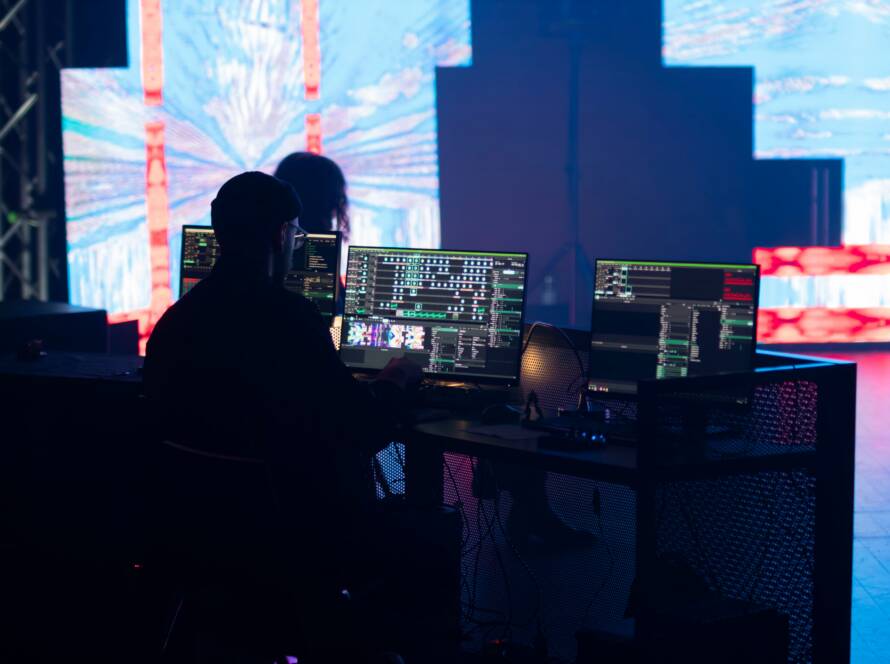 Technician silhouetted at control monitors in front of a large LED video wall