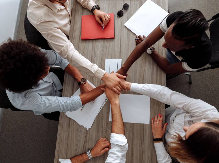 Overhead view of four colleagues stacking hands together over a meeting table