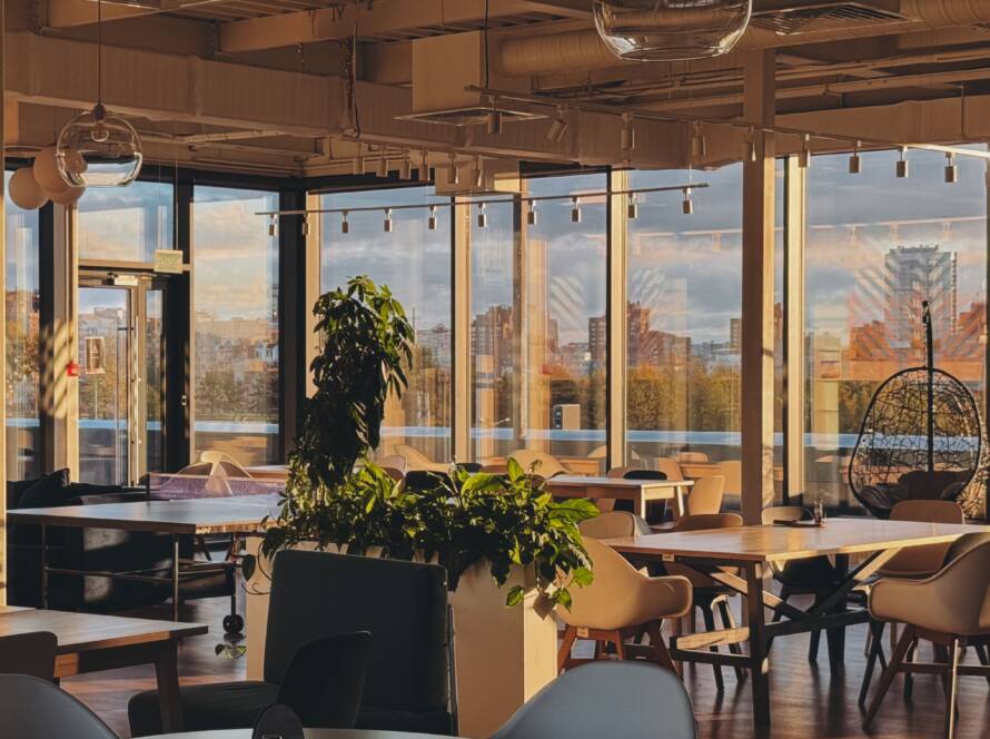 Modern office café with round tables, pendant lights, plants and large windows
