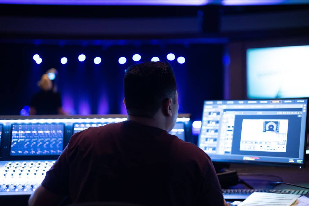 Audio engineer at a mixing console and monitors facing a lit stage