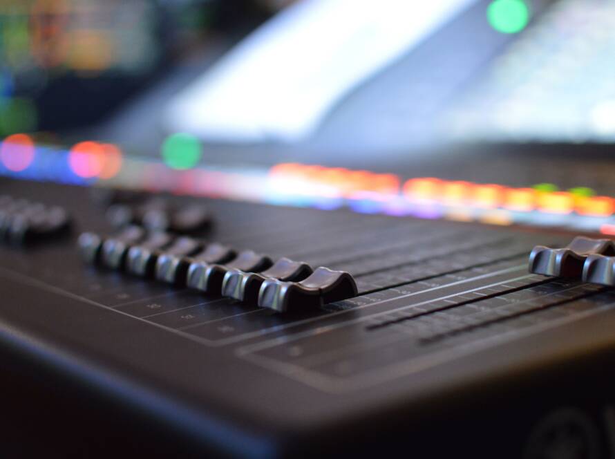 Close-up of faders on an audio mixing console with colored lights