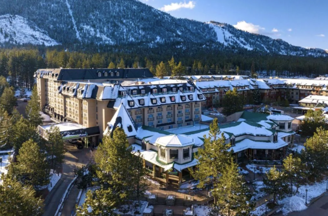Snow-covered mountain resort hotel surrounded by pine trees with ski slopes behind
