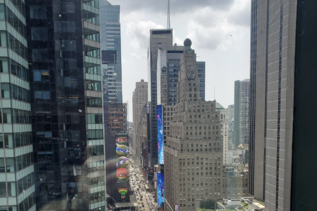 View down a Midtown Manhattan avenue lined with skyscrapers and digital billboards from a high window