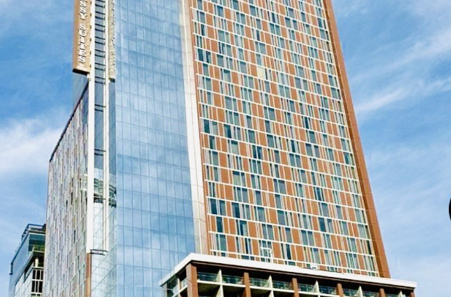 High-rise hotel tower with glass curtain wall and orange-and-gray panel facade against a blue sky