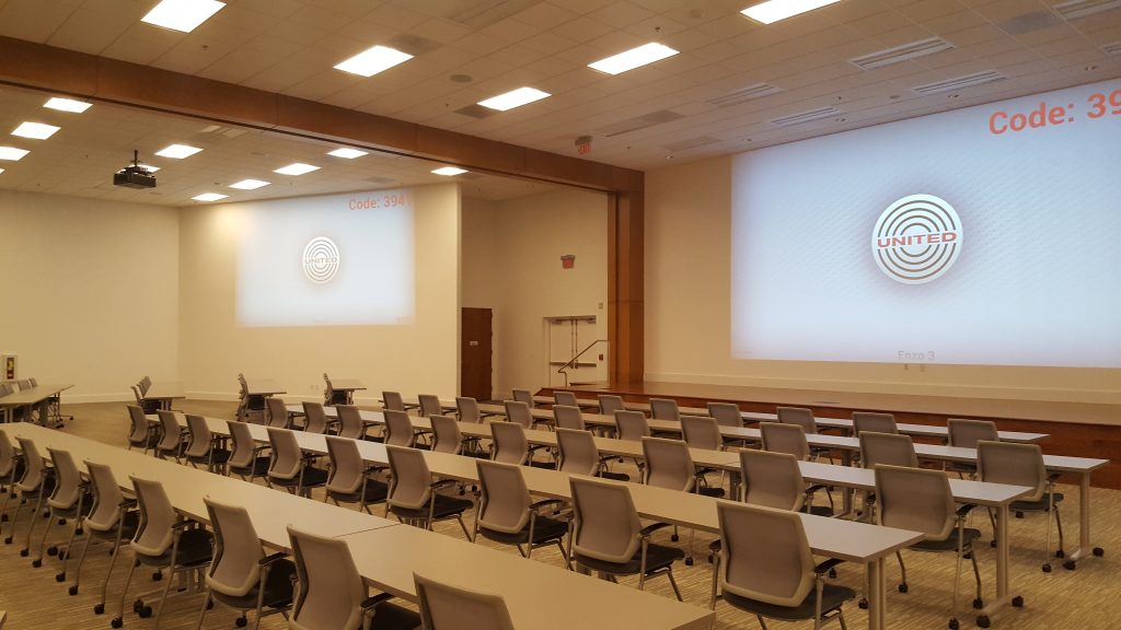 Large training room with rows of tables and chairs facing two projection screens