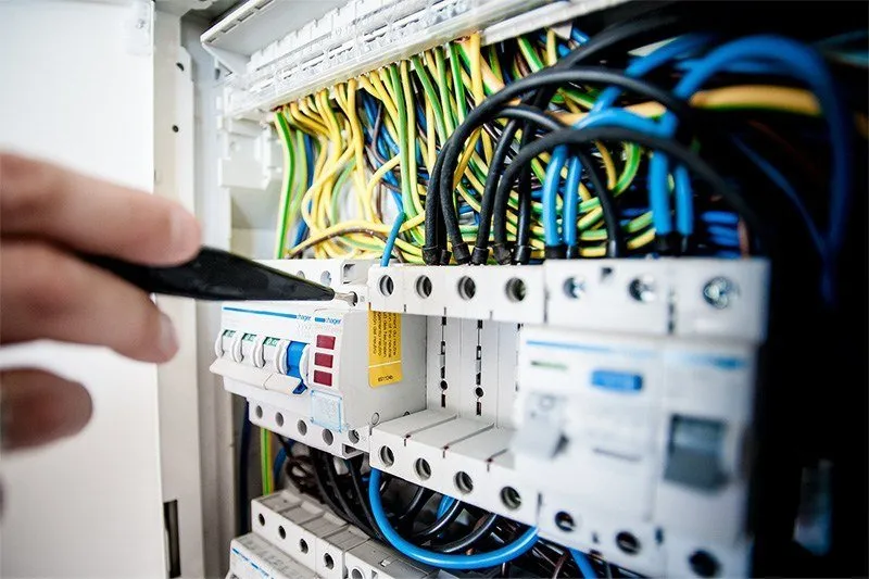 Technician testing wiring in an electrical panel with a screwdriver