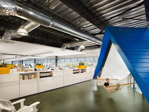 HomeAway office interior with open workspace, exposed ductwork and a hammock under a blue A-frame structure