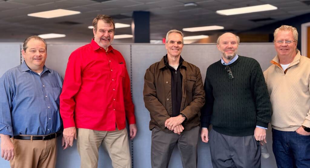Five men standing together smiling in an office