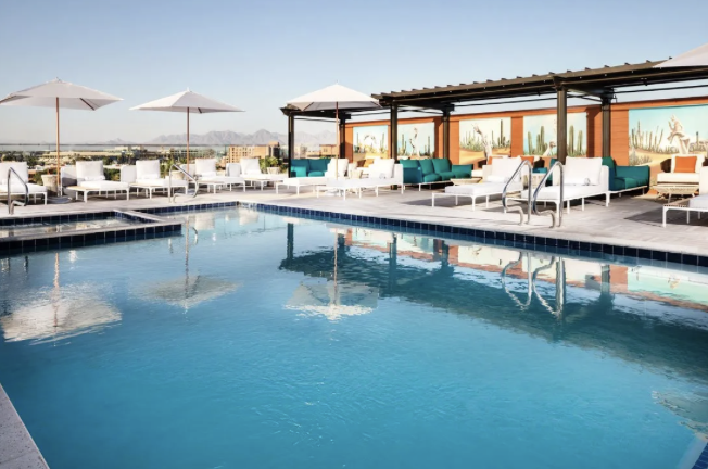 Rooftop pool with white loungers, umbrellas and cabanas under a clear sky