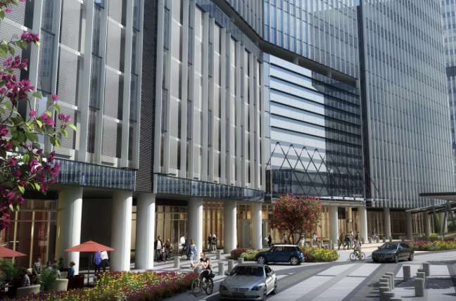 Street-level view of glass office towers with landscaped plaza and cars