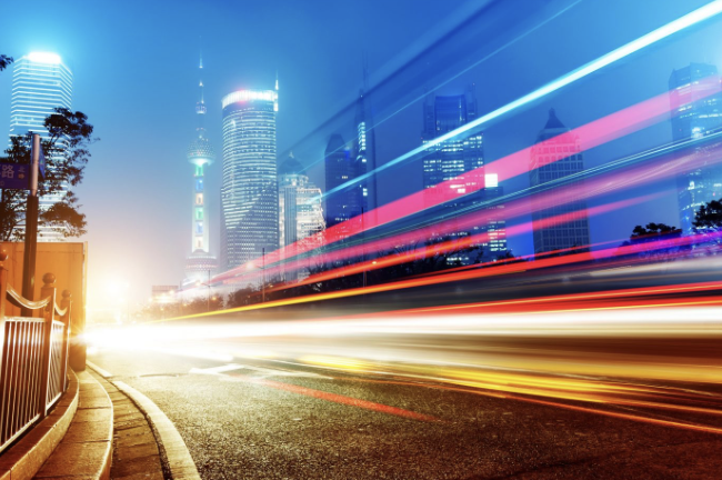 City skyline at night with colorful light trails streaking along a road