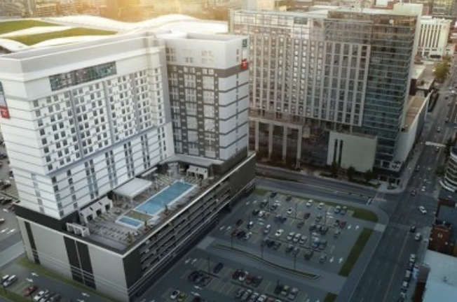 Aerial view of a downtown high-rise hotel with a rooftop pool beside parking lots