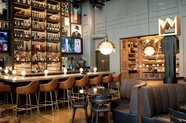 Hotel bar with backlit liquor shelves, leather stools, booths and pendant lights