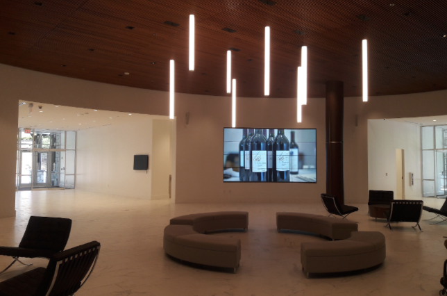 Open lobby with pendant tube lights, curved seating and a large wall display