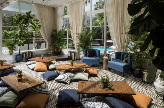 Hotel lounge with tropical plants, floor cushions and low wooden tables beside poolside windows
