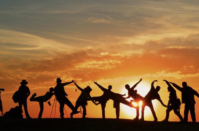 Silhouettes of a group of people posing playfully against an orange sunset