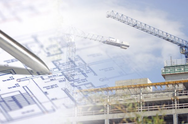 Pen over building blueprints overlaid on a construction site with tower cranes