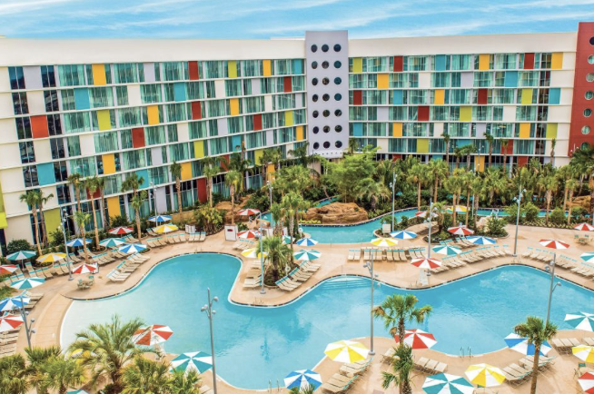 Aerial view of a colorful resort hotel with winding pools, palm trees and umbrellas
