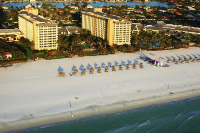 Aerial view of beachfront resort towers overlooking a white sand beach lined with cabanas