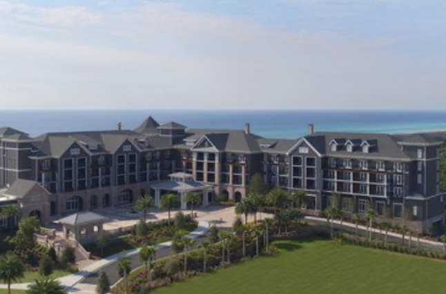 Aerial view of a large gray-shingled beachfront resort with lawns and the ocean behind