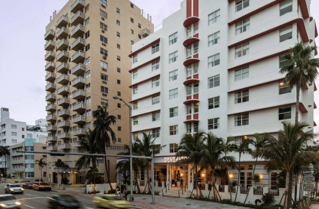 Art Deco Generator hostel building on a Miami Beach street corner with palm trees, beside a residential tower