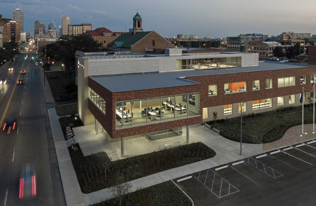 Aerial dusk view of a modern brick and glass office building with parking lot and city skyline behind