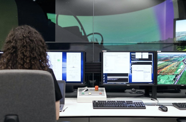 Operator at a control room workstation with multiple monitors and a large curved display