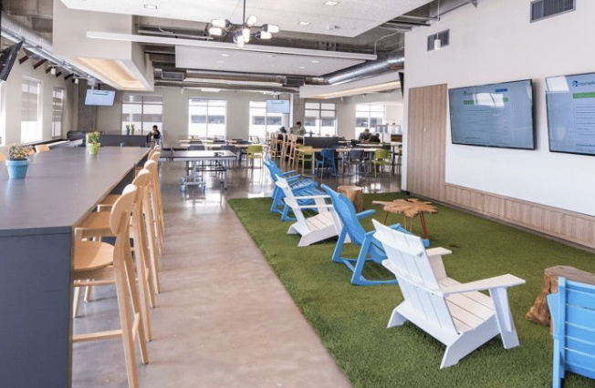 Open office break area with a long counter, bar stools and Adirondack chairs on artificial turf