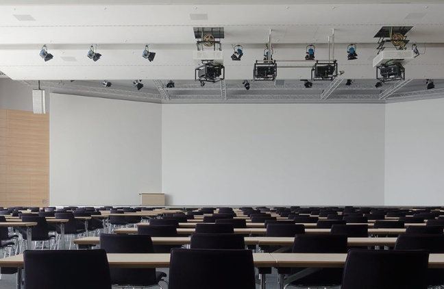 Empty lecture hall with rows of desks and ceiling-mounted projectors and lights
