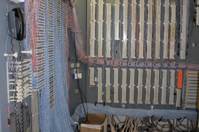 Wall of legacy telephone punch-down blocks with dense, tangled cabling