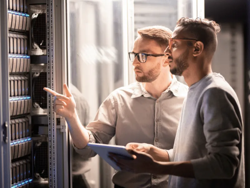 Two IT professionals with a tablet inspecting servers in a data center