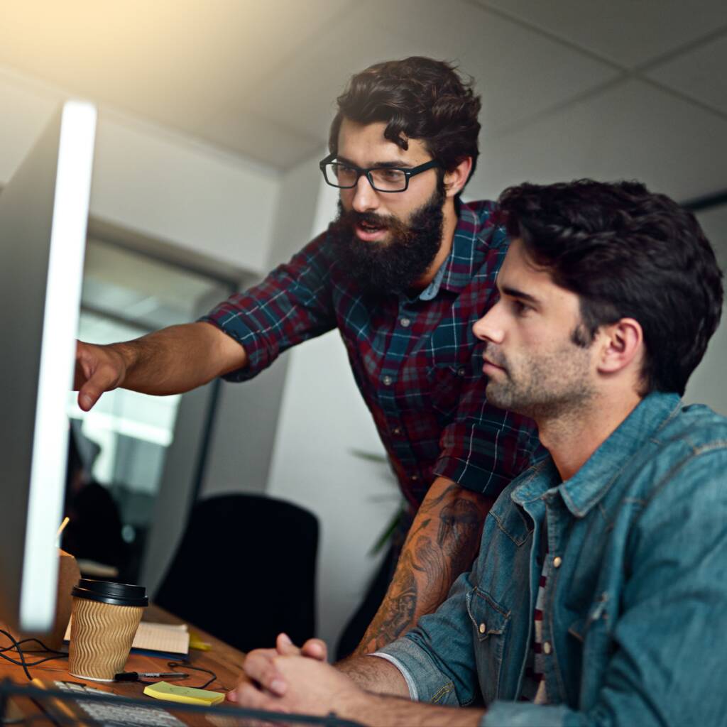 Two colleagues collaborating at a desktop computer, one pointing at the screen
