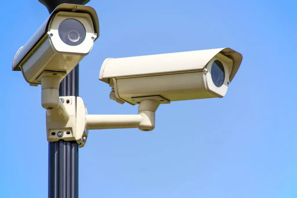 Two security cameras mounted on a pole against a blue sky