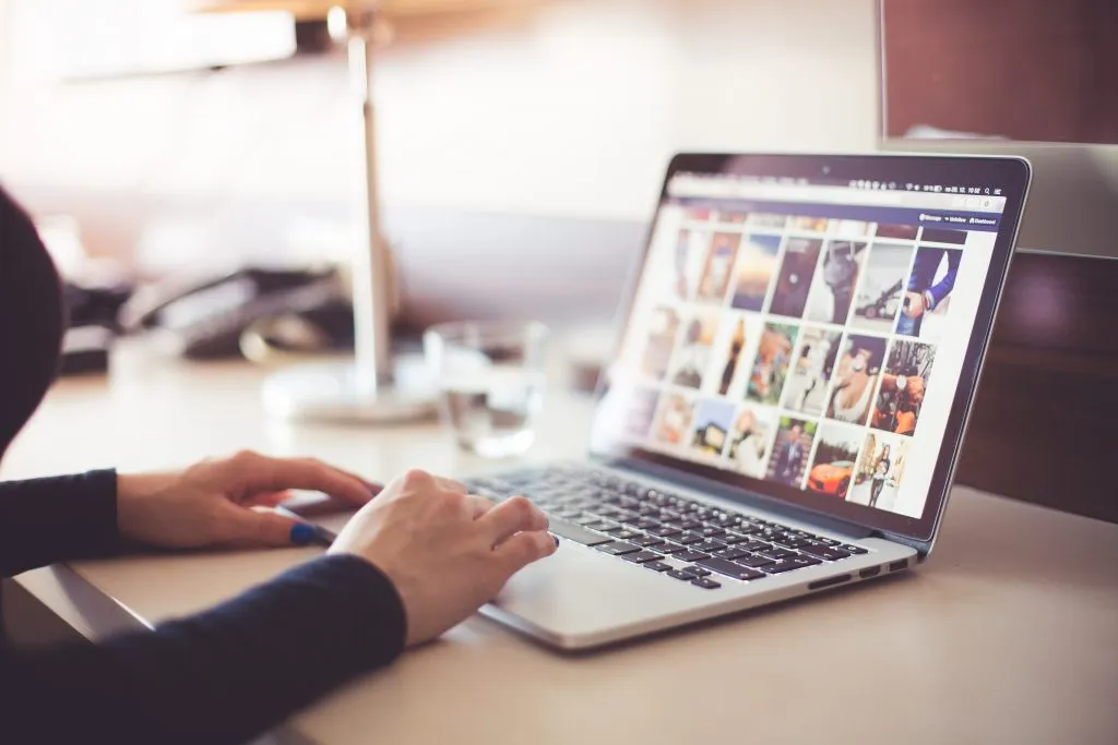 Hands typing on a laptop showing a grid of photos