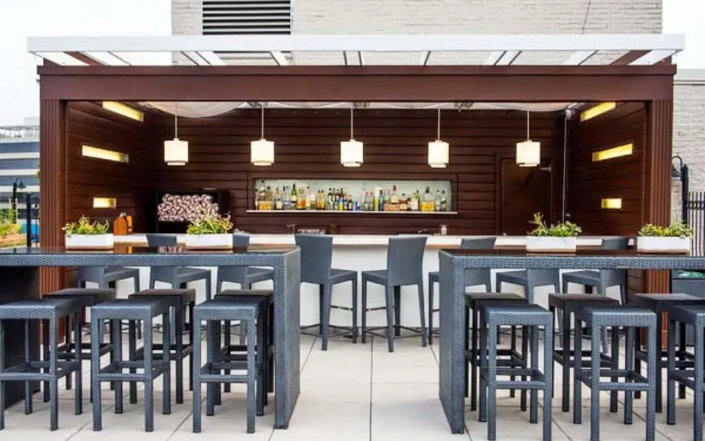 Rooftop pool bar with wood-paneled backbar, pendant lights and high-top seating