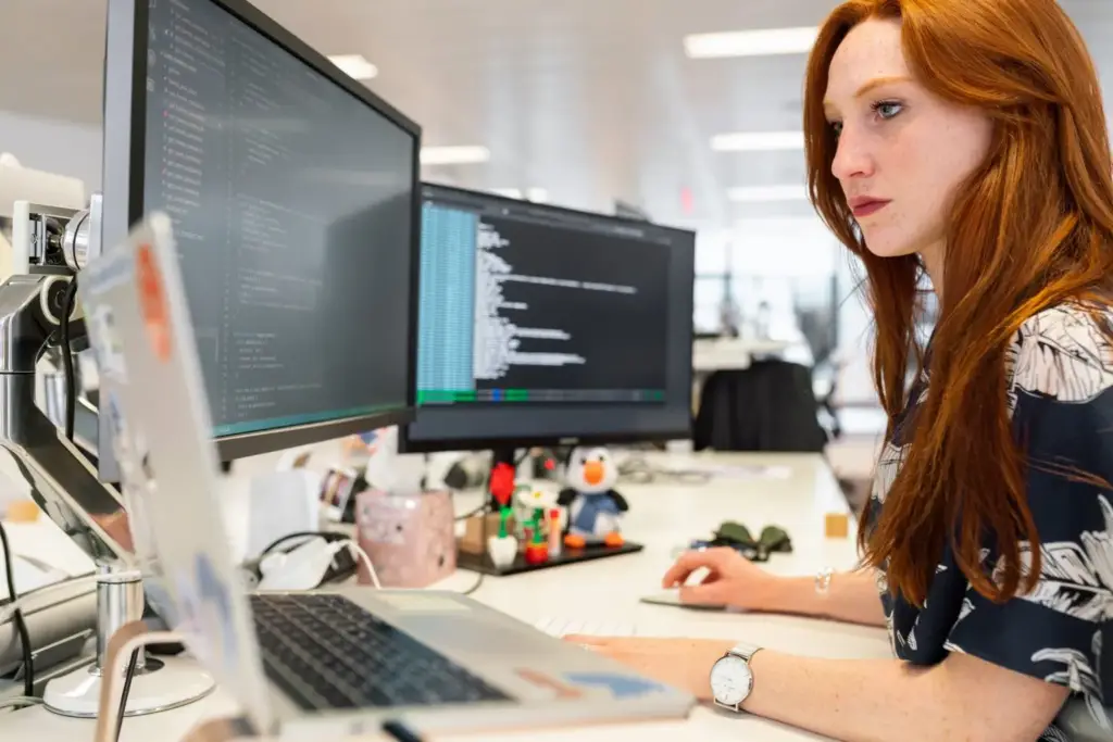 Woman working at a desk with multiple monitors showing code
