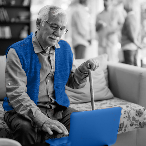 Senior man in a blue vest using a blue-highlighted laptop in a black-and-white living room