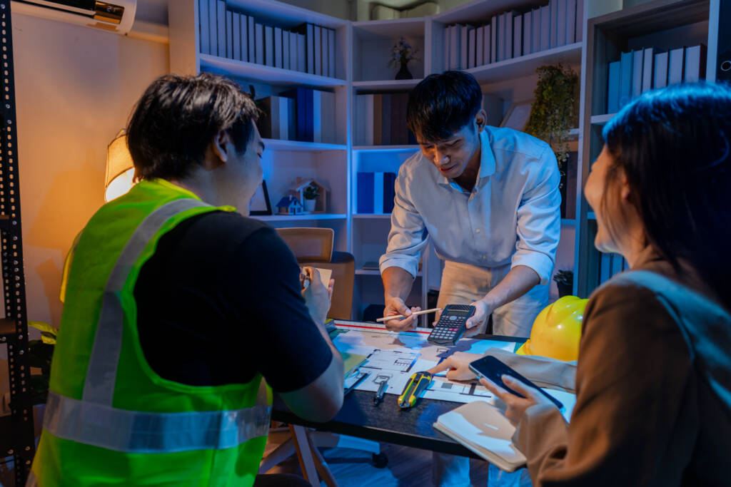 Diverse team discussing architectural plans at a desk, with a worker in a safety vest