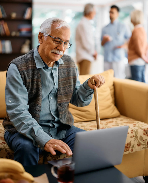 Senior man with a cane using a laptop on a sofa in a senior living community